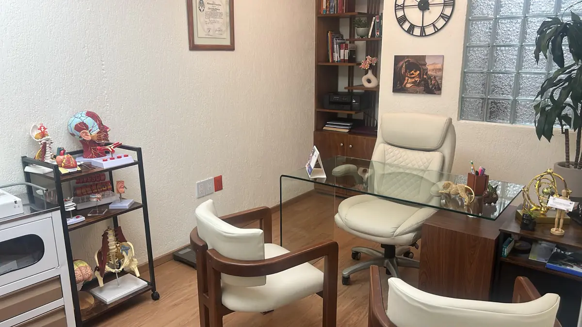 Consultorio de medicina interna de la Dra. Mia Vázquez en el Hospital Ángeles Pedregal con escritorio de vidrio, sillas para pacientes y modelos anatómicos